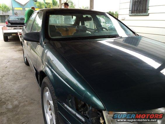 Dark green sedan with missing headlight, on a trailer