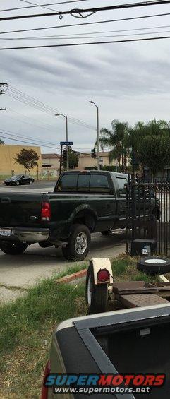 Dark green Ford F-250 pickup truck parked next to a fence. A small trailer is in the foreground