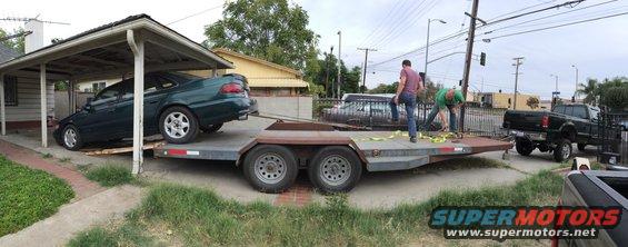 Green sedan on a car trailer, being towed by a black pickup truck