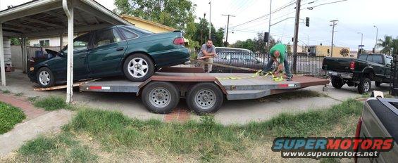 Green sedan being loaded onto a trailer, with a pickup truck attached