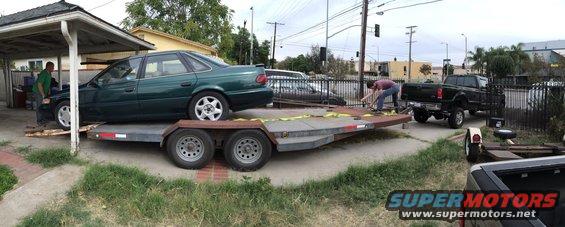 Green 1993 Ford Taurus sedan being loaded onto a trailer, with a black pickup truck nearby