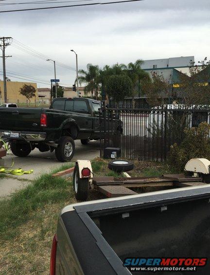 Dark green pickup truck parked next to a trailer. Another truck bed is in the foreground