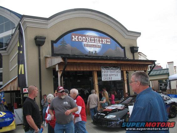Black racing car with colorful decals and "MOONSHINE" text on the side, parked in front of a building