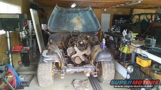 Jeep CJ in garage, hood open, engine out. Another Jeep front end visible to the right