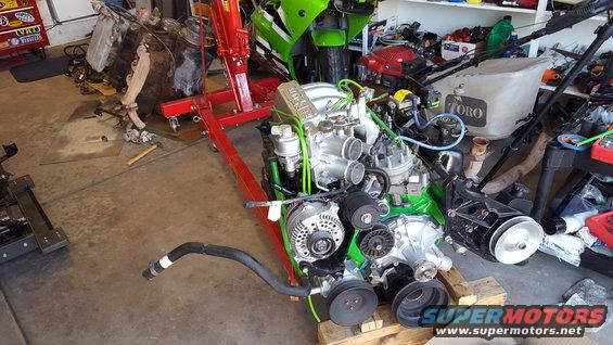 Engine on a red engine stand, with a green motorcycle in the background