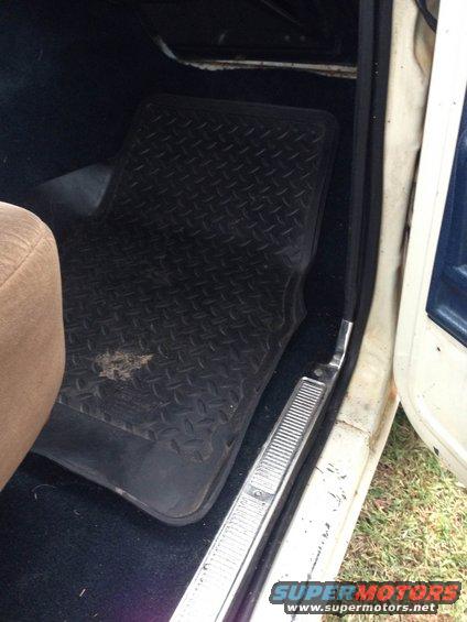 Interior view of a vehicle showing a black rubber floor mat and a tan seat