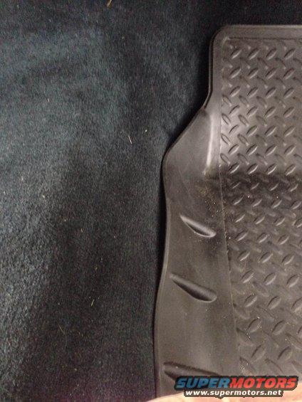 Close-up of a black rubber floor mat with diamond tread pattern on dark carpet