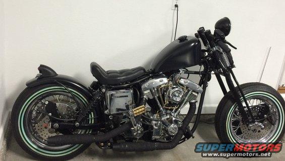 Black custom motorcycle with whitewall tires and exposed engine. Side view