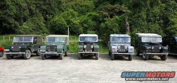 Five vintage Land Rovers parked outdoors with trees in the background. License plates are visible
