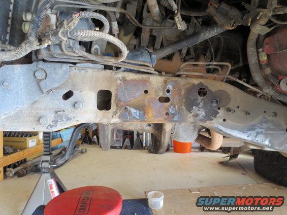 Underside of a vehicle showing rusty frame rails, suspension components, and wiring harnesses