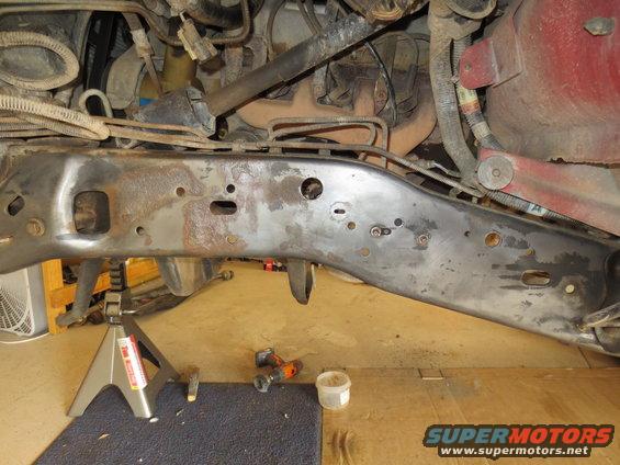 Vehicle frame and engine parts on jack stands, showing rust and wiring