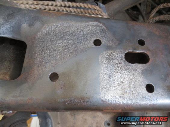 Close-up of a rusty metal vehicle frame section with several holes
