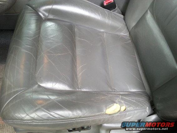 Gray leather driver's seat with visible wear and a large tear on the right side
