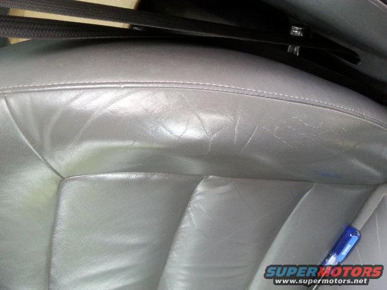 Close-up of a gray leather car seat with visible wear and creasing. A black seatbelt is visible above the seat