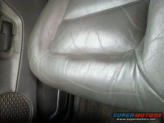 Close-up of a worn black leather driver's seat with visible creasing. The door panel and speaker grille are on the left