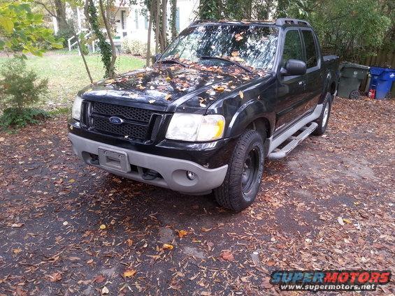 Black 2001 Ford Explorer Sport Trac with leaves on hood, parked on a gravel driveway