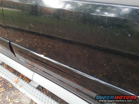 Side of a black SUV showing a running board and some scratches on the lower panel