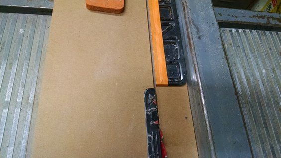 Table saw fence with orange tape and a brown surface
