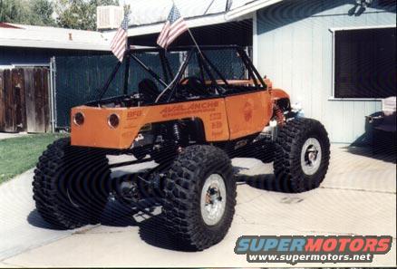 Orange custom off-road vehicle with large tires and roll cage, flying American flags