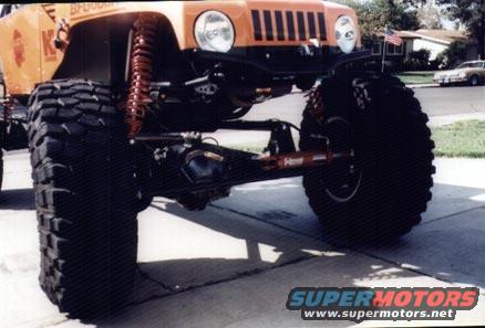 Orange Jeep Wrangler with huge tires and suspension lift, parked on a driveway
