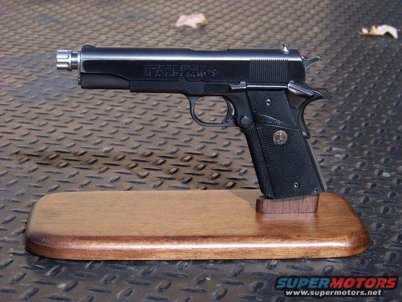 Colt 1911 pistol with threaded barrel, displayed on a wooden base