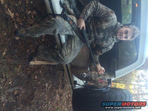 Hunter with rifle and deer in the bed of a white pickup truck