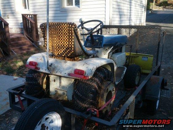 Rear view of a white tractor with chains on tires, loaded on a trailer