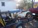 1982 Kubota RTV900 - A white and blue John Deere tractor is secured to a trailer, with a red pickup truck visible behind it.