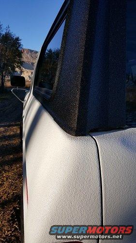 Side view of a truck bed with a textured spray-on liner. A red reflector is visible on the rear corner