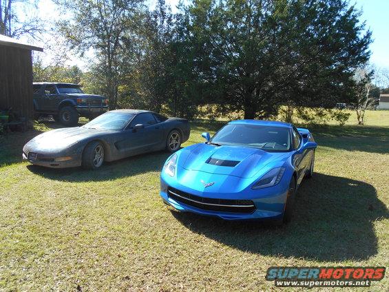 Blue and dark grey Chevrolet Corvettes parked on grass with a Ford Bronco in the background
