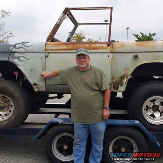 Rusty 1972 Ford Bronco on a trailer, side view, with flame decals on the fender
