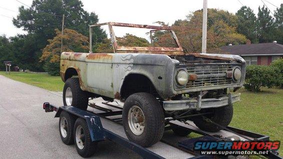 1972 Ford Bronco body on a trailer, front view, heavily rusted, missing windshield and roof