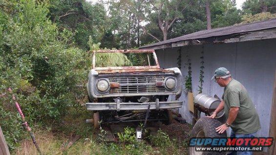 Rusted 1970s Ford Bronco front end, missing windshield and roof, on jack stands