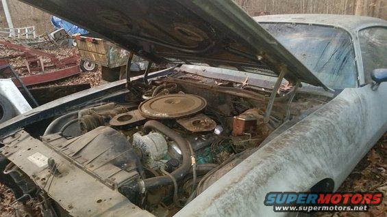 Engine bay of a dusty car with hood open. Watermark reads SUPERMOTORS