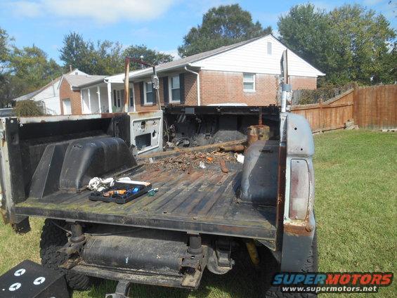 Back of a disassembled pickup truck bed with tools on it, parked in a yard with houses in the background
