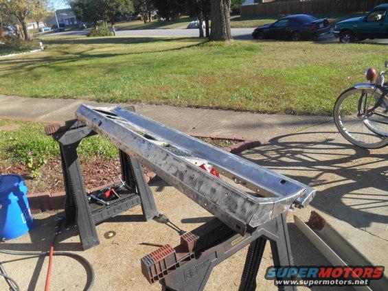 Metal car bumper on sawhorses outdoors, with a bicycle and other cars in the background