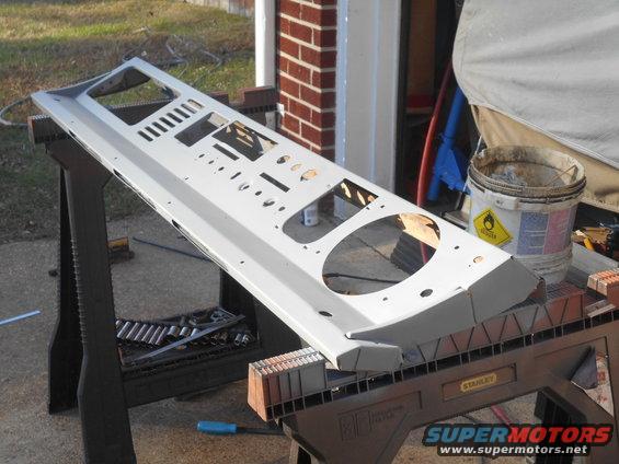 Gray dashboard panel with numerous cutouts for gauges and controls, resting on sawhorses