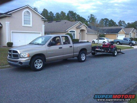 Tan Dodge Ram pickup truck towing a red ATV on a trailer