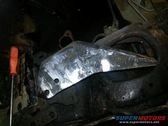 Metal bracket bolted to vehicle frame, with orange-handled screwdriver nearby