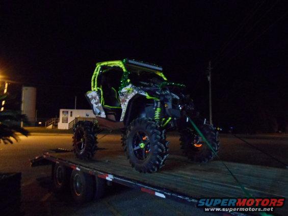 Custom off-road vehicle with neon green roll cage and accents on a flatbed trailer at night
