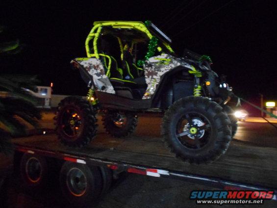 Side-by-side off-road vehicle with camouflage pattern and yellow roll cage on a flatbed trailer at night