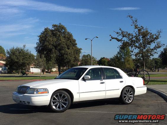 White sedan with aftermarket wheels parked outdoors. A bicycle is mounted on a rack on the rear
