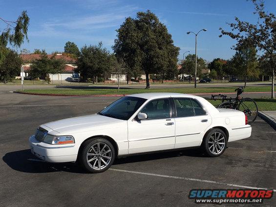 White sedan parked in a lot, side view. Bicycle rack attached to the rear