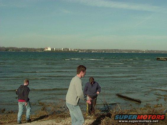 Waterfront scene with three people on a beach, distant buildings on the horizon