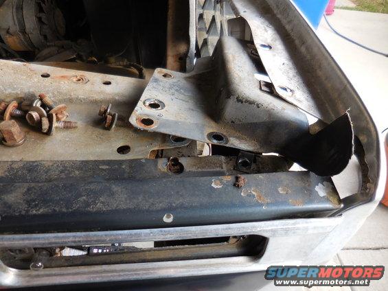 Loose bolts and brackets on a vehicle's front end, showing disassembled parts near the grille
