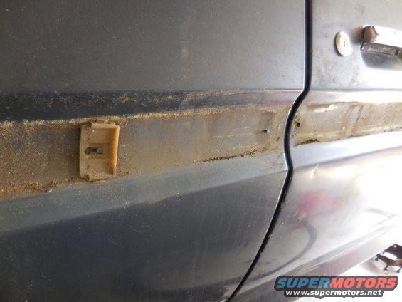 Dark blue car door with a broken beige trim clip and rust buildup along the body line