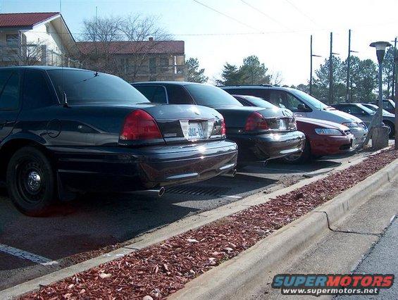 Black police car parked in a lot, rear view. Other cars are parked in line behind it
