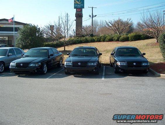 Three black Ford Crown Victorias parked in a lot, one silver car to the left