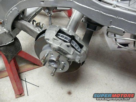 Close-up of a car's front brake caliper, rotor, and suspension assembly on jack stands
