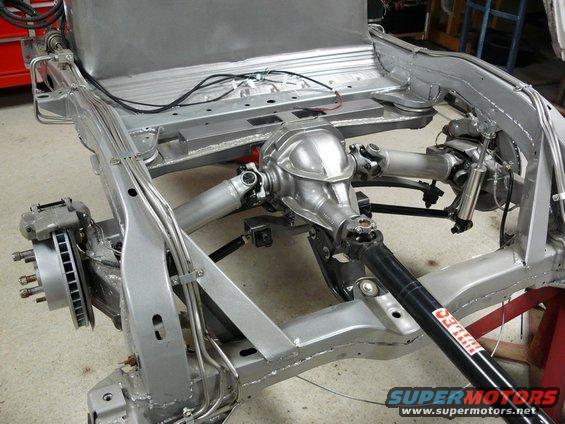Car frame with rear differential, driveshaft, and suspension components visible. Some text on driveshaft